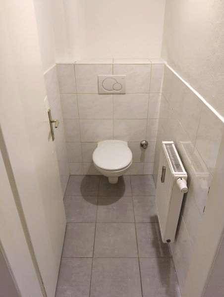 Separates WC mit wandhängender Toilette, Heizkörper und hellen Fliesen an Wänden und Boden.