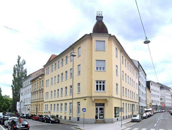 Historisches Eckgebäude mit markantem Dach und vielen Fenstern an einer belebten Stadtstraße.