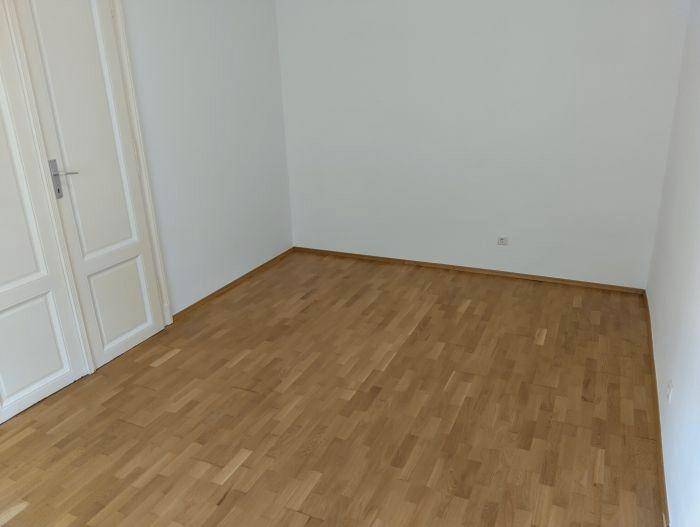 Leerer Raum mit Parkettboden und weiß gestrichenen Wänden, bereit zur individuellen Einrichtung.