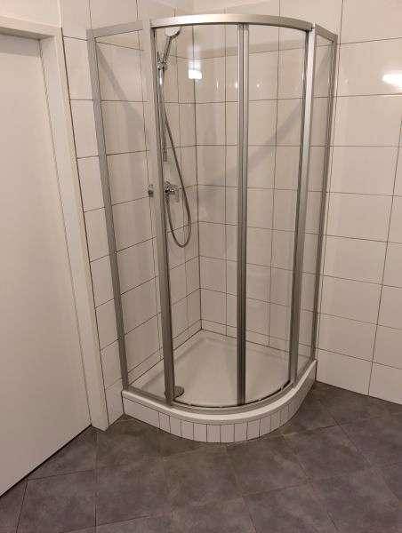 Badezimmer mit weißen Fliesen, grauen Bodenfliesen und einer modernen Eckduschkabine.