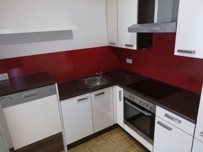 Moderne Küche mit weißen Schränken, roter Rückwand und integrierten Geräten.