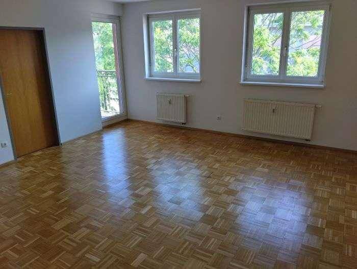Helles Wohnzimmer mit Parkettboden, großen Fenstern und Zugang zum Balkon.