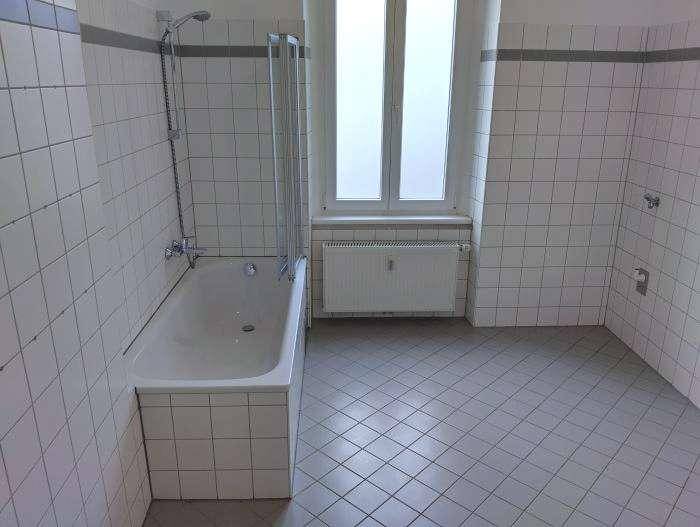 Helles Badezimmer mit weißen Fliesen, Badewanne mit Duschfunktion und Fenster.