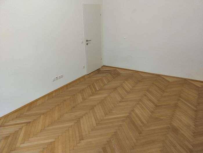 Leerer Raum mit elegantem Fischgrätparkettboden und weißer Tür, vielseitig nutzbar.