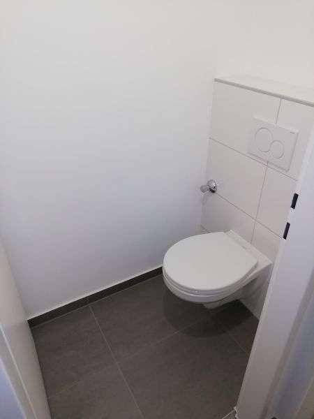 Separates WC mit wandhängender Toilette und modernen Fliesen in Grau und Weiß.