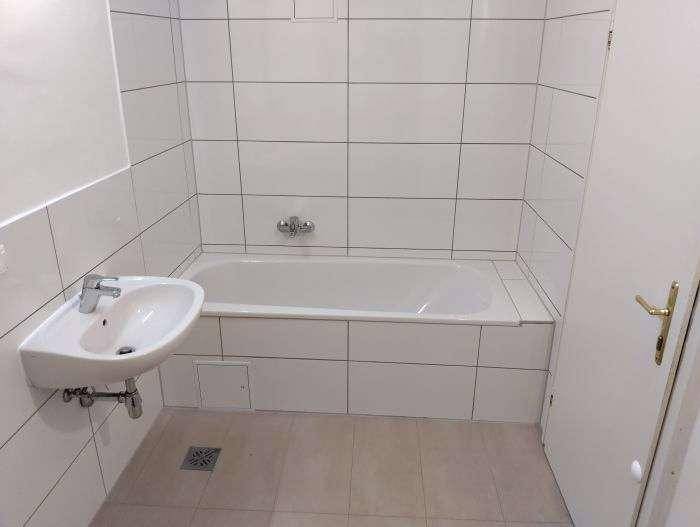 Modern gefliestes Badezimmer mit Badewanne und wandmontiertem Waschbecken in Weiß.