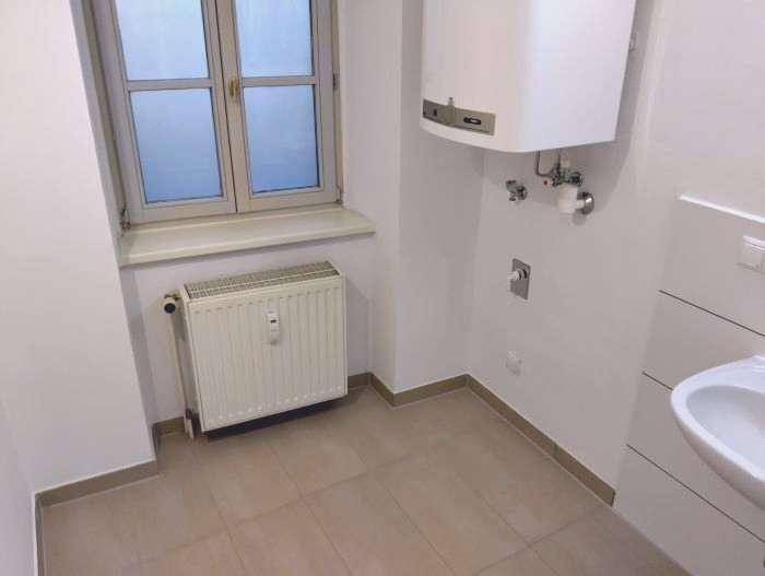 Badezimmer mit Fenster, Heizkörper und Warmwasserbereiter, bietet grundlegende Ausstattung.