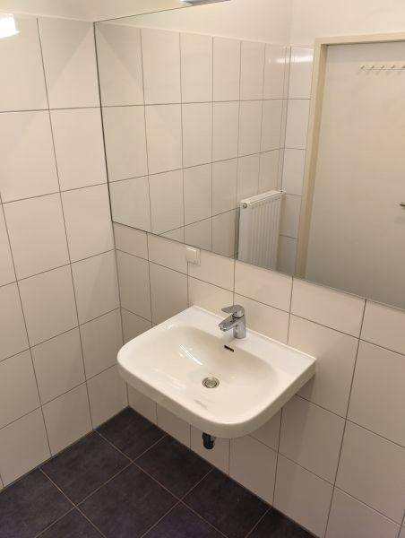 Badezimmer mit modernem Waschbecken, großem Spiegel und weißen Wandfliesen auf dunklem Boden.