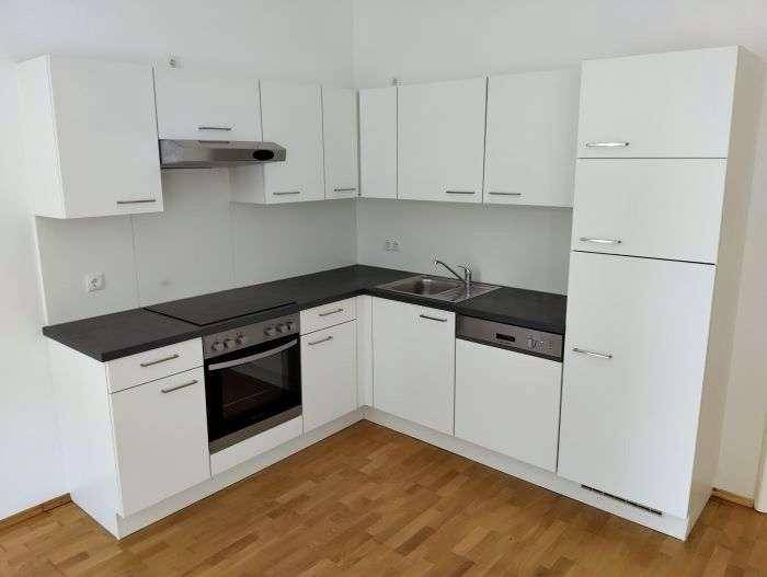 Moderne Einbauküche mit weißen Fronten, integrierten Geräten und dunkler Arbeitsfläche.