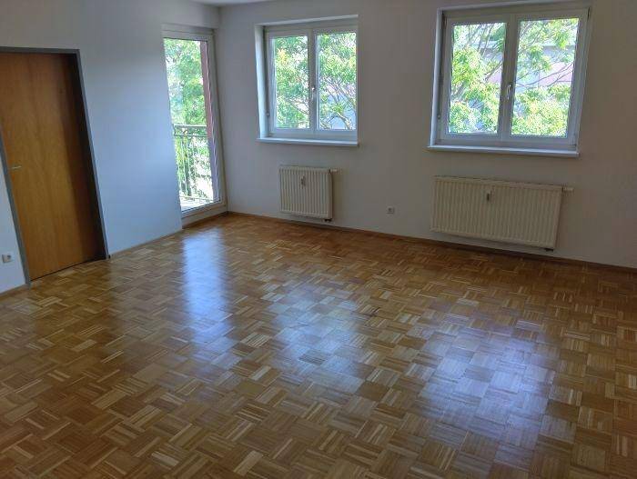 Helles Zimmer mit Parkettboden, großen Fenstern und Zugang zu einem französischen Balkon.