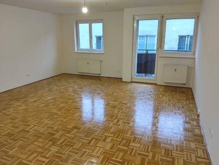 Helles Wohnzimmer mit glänzendem Parkettboden und Zugang zu einem kleinen Balkon, gut gepflegt.