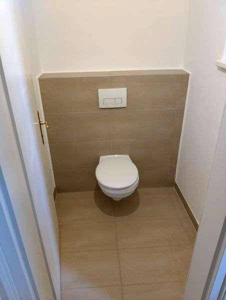 Separates WC mit wandhängender Toilette und modernen Fliesen an Wänden und Boden.