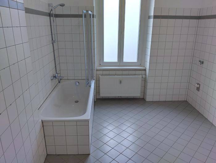 Helles Badezimmer mit weißen Fliesen, Badewanne und Fenster für natürliches Licht.
