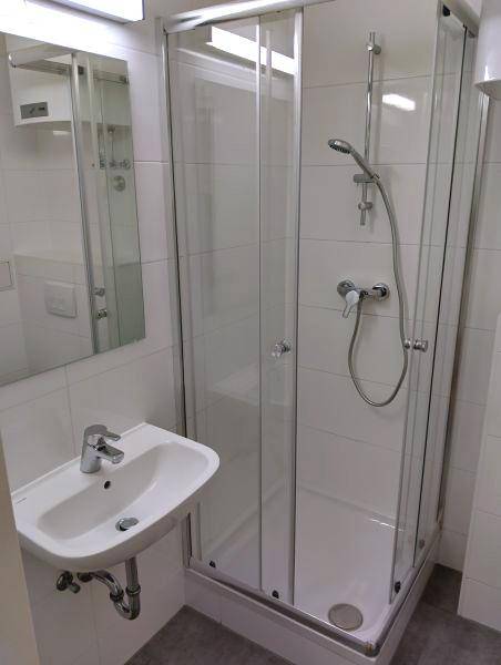 Modernes Badezimmer mit Duschkabine, Waschbecken und weißen Wandfliesen, funktional und sauber.