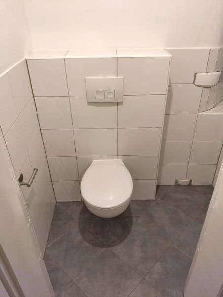 Separate Toilette mit wandhängendem WC und weißen Fliesen an den Wänden.