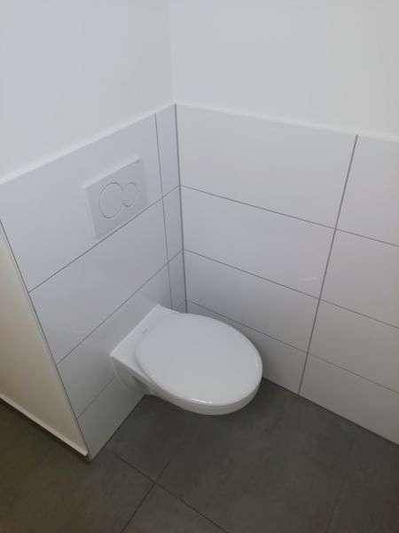 Sauberes WC mit wandhängender Toilette und modernen Fliesen an Wänden und Boden.