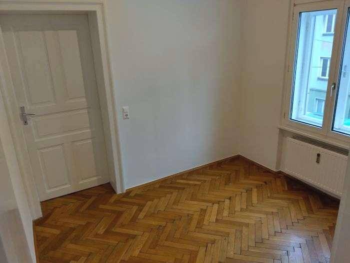 Heller Raum mit klassischem Fischgrätparkett, großen Fenstern und einer traditionellen weißen Tür.