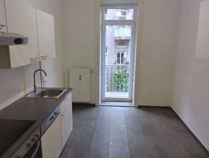 Funktionale Küche mit weißen Schränken, dunkler Arbeitsplatte und Zugang zu einem französischen Balkon.