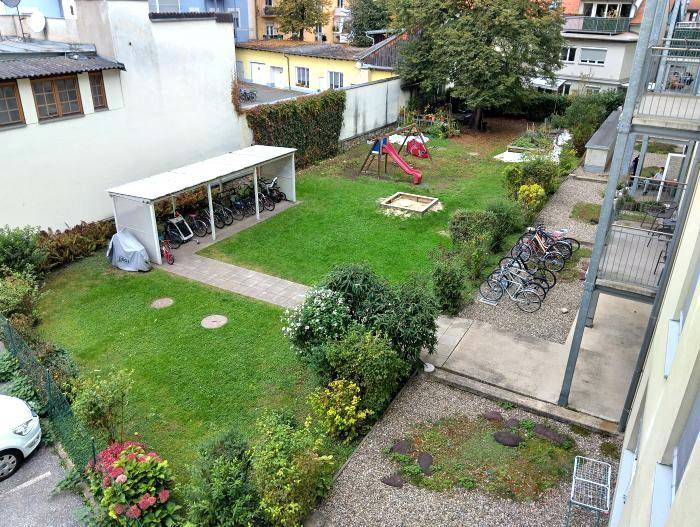 Gemeinschaftsgarten mit Rasenfläche, Spielplatz und überdachtem Fahrradabstellplatz.