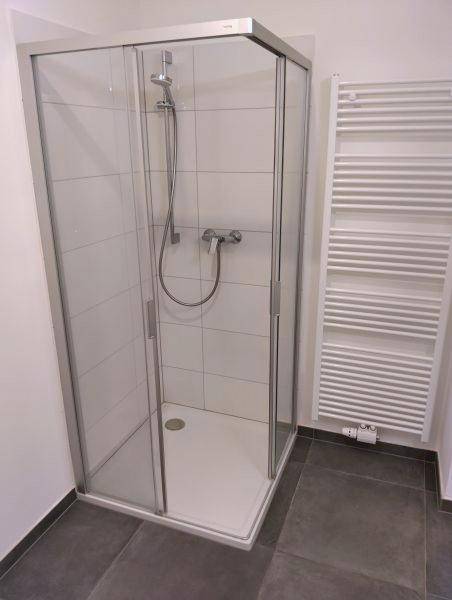 Moderne Duschkabine mit Glaswänden, weißen Fliesen und dunklem Boden in einem Badezimmer.