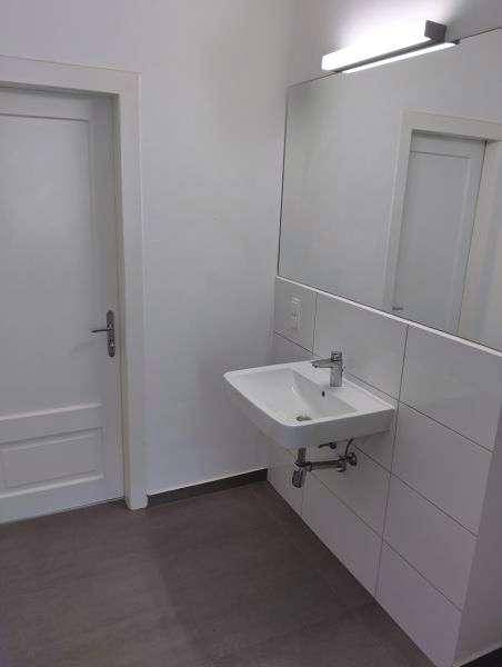 Modernes Badezimmer mit weißem Wandwaschbecken, großem Spiegel und hellen Wandfliesen.