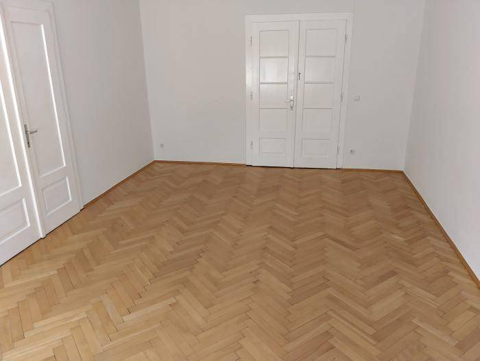 Geräumiges Zimmer mit klassischem Fischgrätparkett und zwei weißen Flügeltüren.