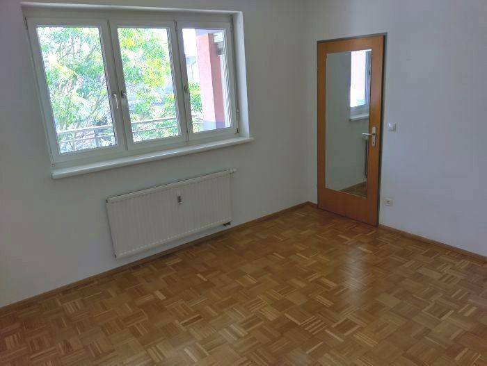 Helles Zimmer mit Parkettboden, großem Fenster und einer Tür mit Spiegelfläche.
