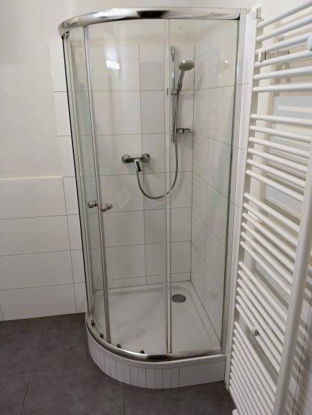 Badezimmer mit einer Eckduschkabine, weißen Wandfliesen und einem praktischen Handtuchheizkörper.