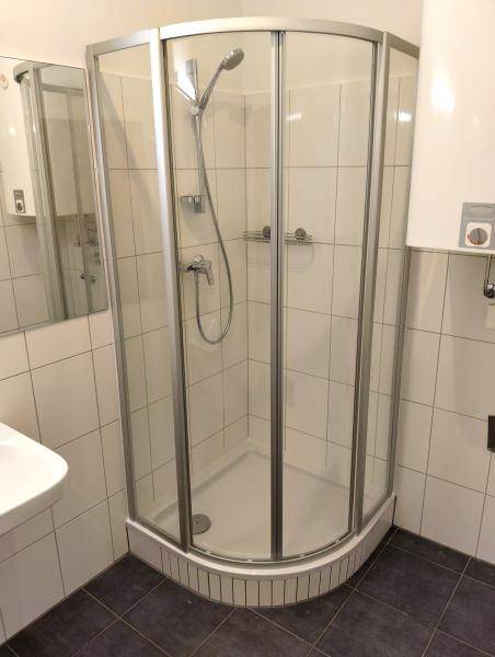 Modernes Badezimmer mit Eckduschkabine, weißen Wandfliesen und dunklem Fliesenboden.