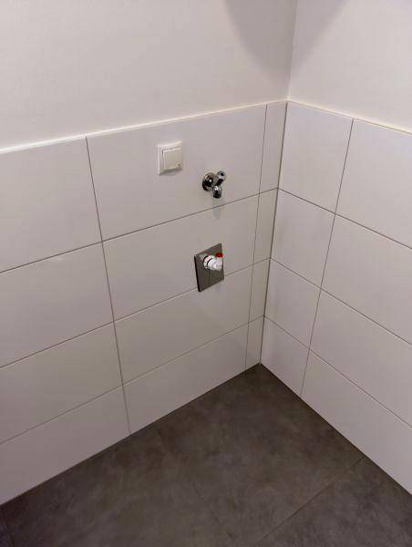 Gefliester Bereich mit Anschlüssen für eine Waschmaschine, ideal als Hauswirtschaftsraum nutzbar.