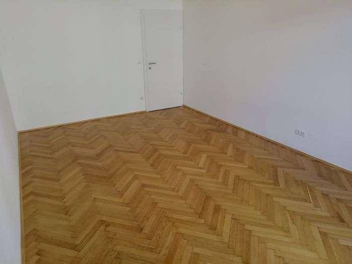Leeres Zimmer mit elegantem Fischgrätparkett und einer weißen Tür, ideal für individuelle Gestaltung.
