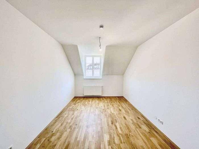 Helles Schlafzimmer in Dachgeschosswohnung mit Holzboden, schrägen Wänden und Fenster.