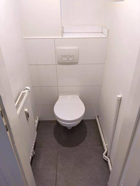 Separates WC mit wandhängender Toilette, weißen Fliesen und einem Heizkörper.