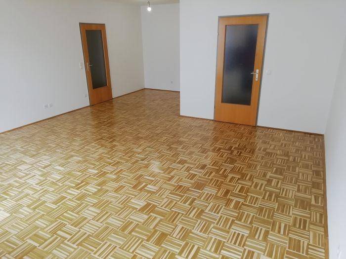 Geräumiger Raum mit hellem Parkettboden und zwei Holztüren, bereit zur individuellen Einrichtung.
