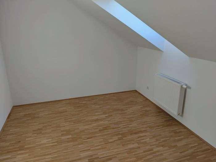 Helles Zimmer im Dachgeschoss mit Parkettboden, Dachfenster und Heizkörper.