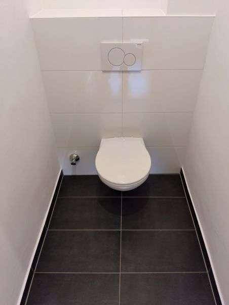Separate Toilette mit wandhängendem WC und dunklen Bodenfliesen in einem schlichten Design.