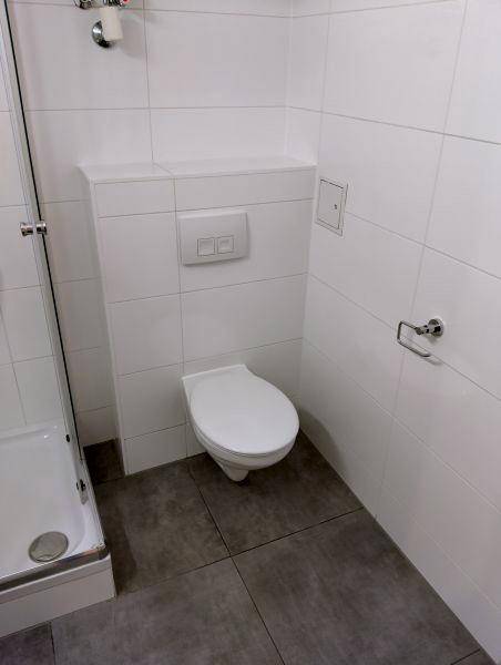 Sauberes Badezimmer mit wandhängender Toilette und grauen Bodenfliesen, passend zum modernen Stil.