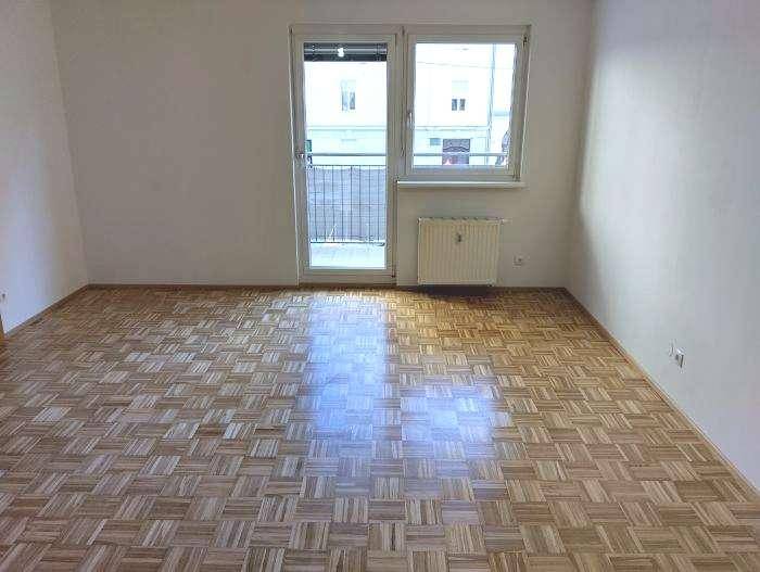 Heller Wohnraum mit Parkettboden und Zugang zu einem kleinen Balkon.