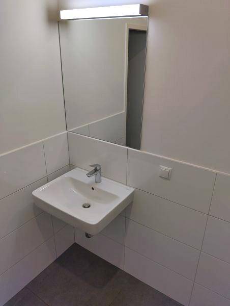 Modernes Waschbecken mit Spiegel und Beleuchtung in einem hell gefliesten Badezimmerbereich.