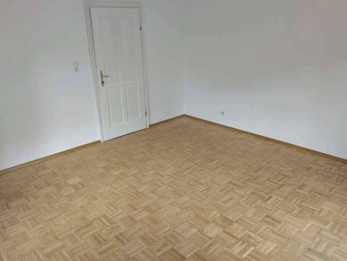Leeres Zimmer mit Parkettboden und einer weißen Tür, bereit zur Einrichtung.