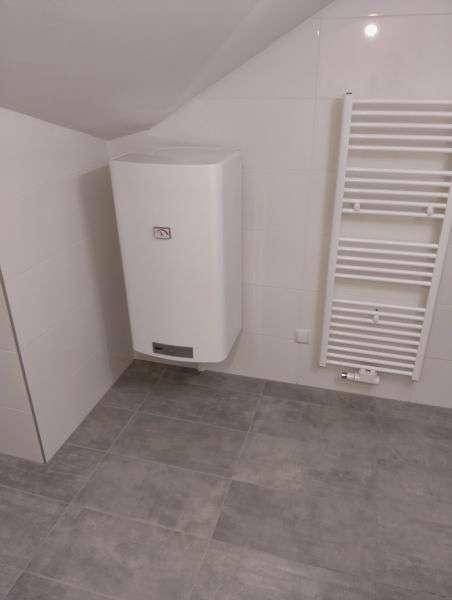 Badezimmer mit Handtuchheizkörper und Warmwasserboiler, gefliest in hellen Farbtönen.