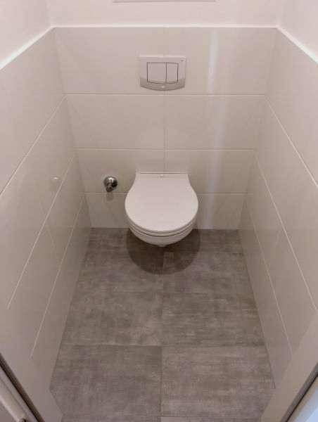 Separates WC mit wandhängender Toilette und modernen Fliesen an Wänden und Boden.
