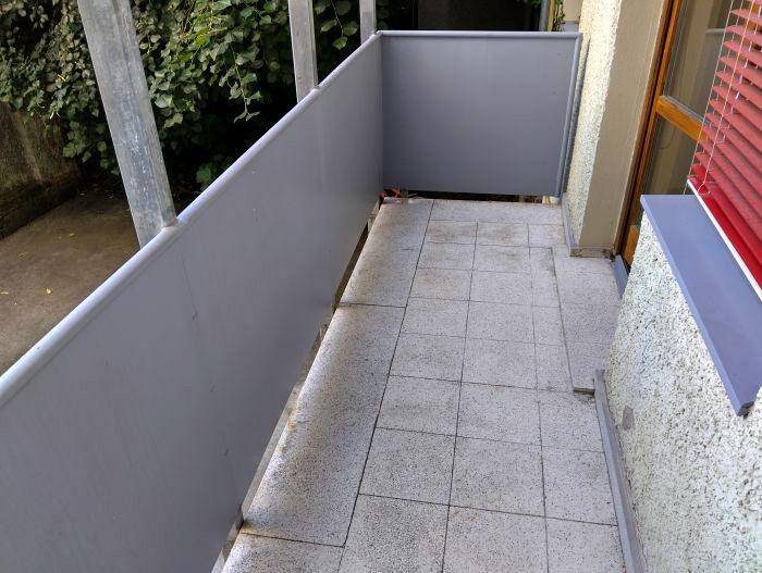 Balkon mit Fliesenboden und Blick ins Grüne, umgeben von einer grauen Brüstung.
