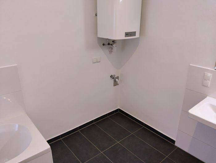 Ecke eines Badezimmers mit Warmwasserbereiter und dunklen Bodenfliesen.