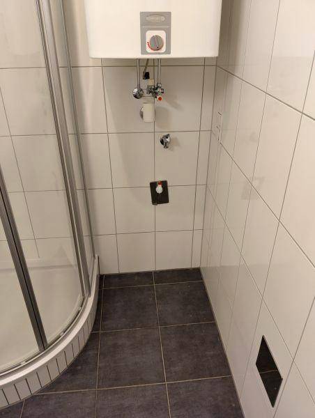 Badezimmerbereich mit weißen Wandfliesen, dunklem Boden und einem Warmwasserbereiter.