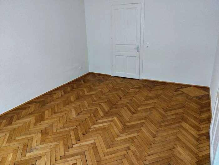Geräumiges Zimmer mit elegantem Fischgrätparkett und einer klassischen weißen Tür, ideal für individuelle Gestaltung.