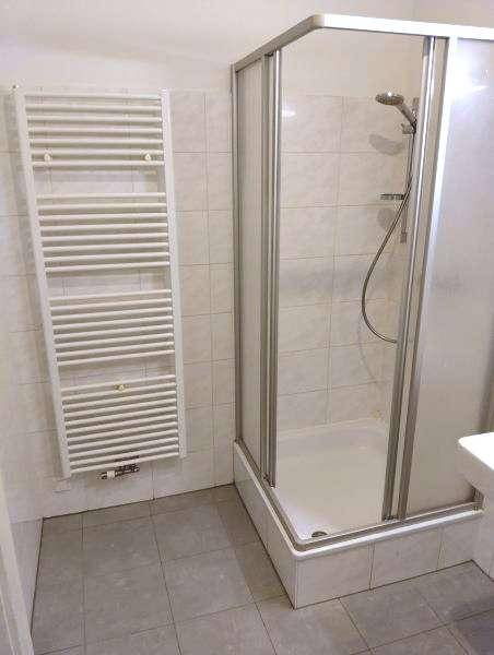 Funktionales Badezimmer mit Duschkabine, beheiztem Handtuchhalter und hellen Fliesen an Wänden und Boden.