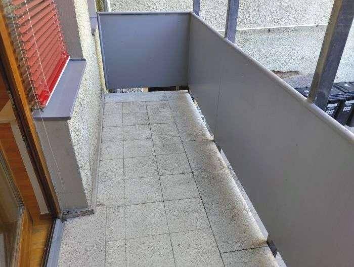 Schmaler Balkon mit Fliesenboden und grauen Brüstungselementen, ideal für kleine Pflanzen.