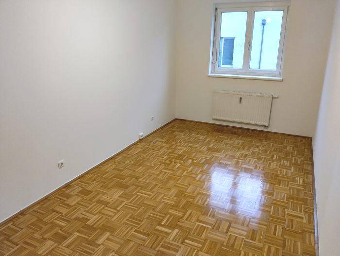 Helles Schlafzimmer mit Parkettboden und großem Fenster, ideal für natürliche Beleuchtung.