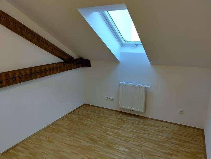 Dachzimmer mit Holzbalken, Parkettboden und einem großen Dachfenster für viel Licht.